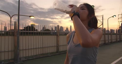 Young Asia athlete lady exercises drinking water because feel tired after running in city
