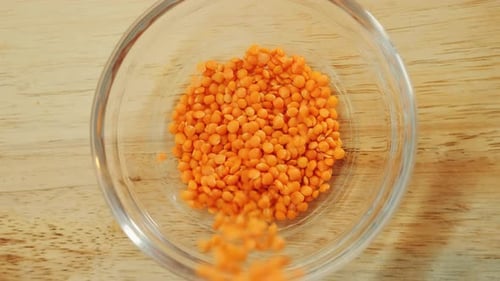 Bright Orange Lentils Being Poured Into Clear Bowl