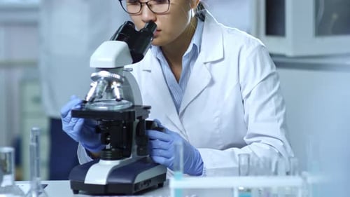 Young Scientist Looks into a Microscope in Lab