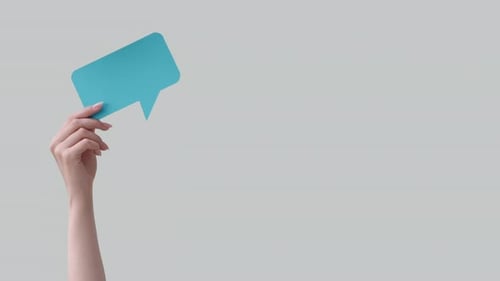 Hand Holding Teal Speech Bubble Against Gray Background