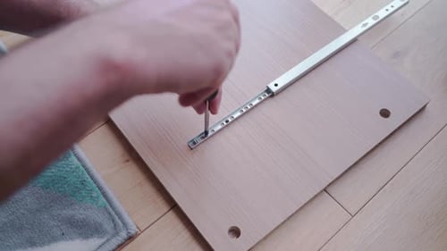 Man installing drawer slides on an element of a chest of drawers with a screwdriver and tests it on