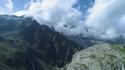 Moving Backward Over Alpine Rocks Revealing Mountain Valley in Sunny Summer with Clouds