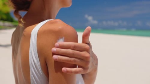 Close Up of a Happy Smiling Young Woman is Applying a Sunscreen or Sun Tanning Lotion on a Shoulder