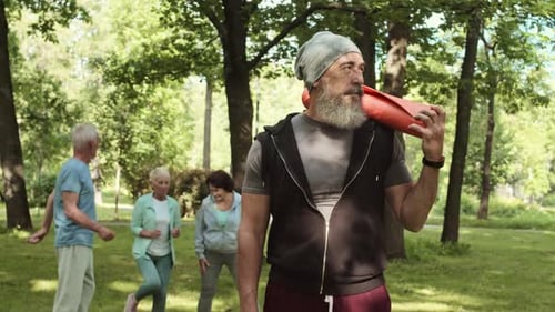 Fitness Instructor with Seniors Exercising Outdoors in Park