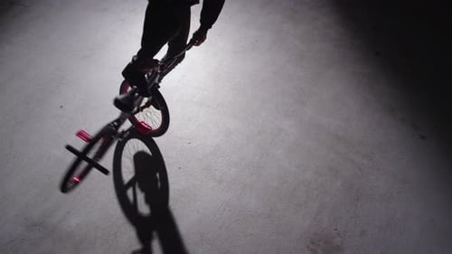 BMX rider doing tricks in dark warehouse.