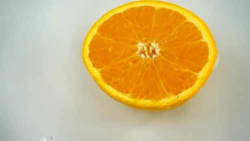 Rotating segment of a ripe and juicy orange in water on an white background. Slow motion.