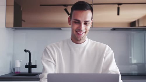 Confident Young Man Sitting at His Desk at Home, Opens and Starts Using Laptop