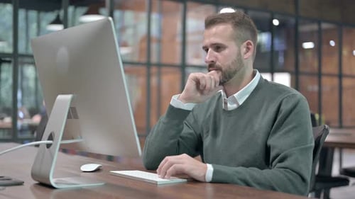 Junger Mann denkt bei der Arbeit am Computer
