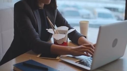 Woman Eating Noodles at Her Workplace with Laptop