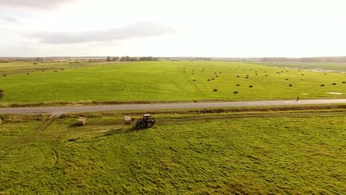 The tractor is stacking haystacks on an agricultural field in autumn, aerial view