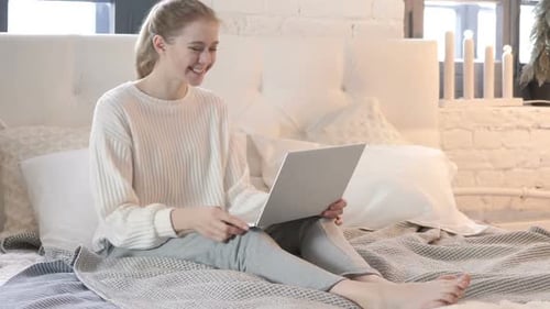 Online-Video-Chat auf dem Laptop von einer jungen Frau, die im Bett sitzt