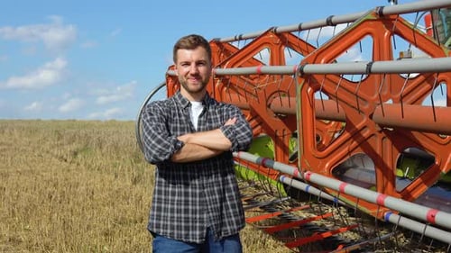 Farmer in Wheat Field with Combine Harvester Harvesting in Background