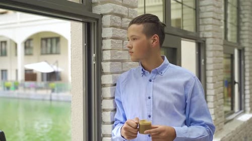 Young Adult Drinks Coffee, Looks out Window