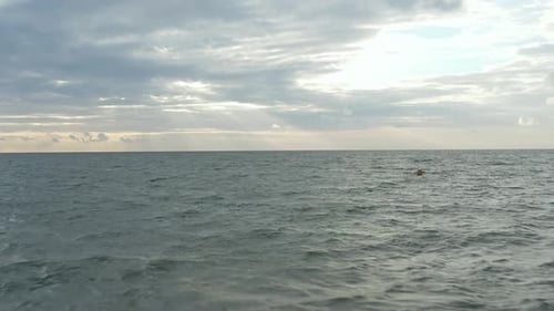 Yellow Buoy in Ruff Ocean with Sunset Cloudscape in Distance, Aerial Forward