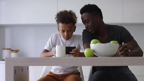 Boy Watches Phone With Man in Kitchen