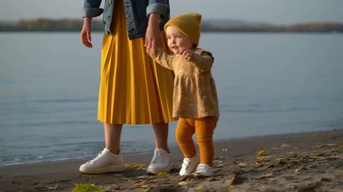 Mom Holds Her Daughter By the Hand and Teaches Her To Walk on Beach