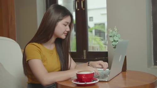 Beautiful Young Asian Girl Working at a Coffee Shop with a Laptop