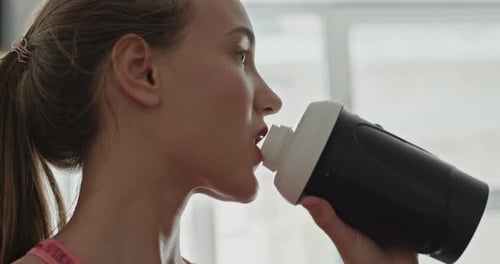 Side View of Young Slim Woman in Sportswear Taking Sip of Water From Training Bottle in Gym.
