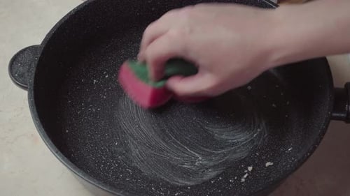 Hand with a foam sponge washes a dirty frying pan. Wash the pan with a sponge