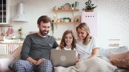 Smiling Happy Family Sitting on Grey Sofa and Using Laptop in Big Living Room with Kitchen on