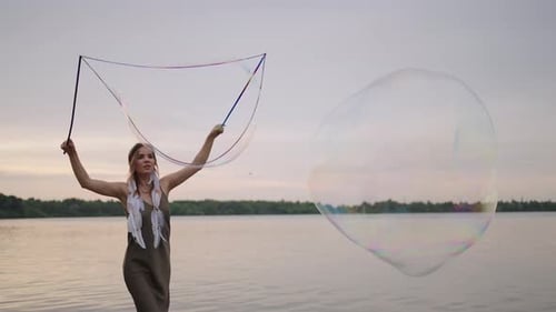 Woman Creates Giant Bubbles by Lake at Sunset
