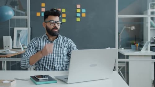 Empleado infeliz de Oriente Medio que usa una computadora portátil, luego golpea la mesa con el puño