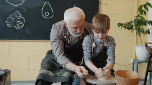 Grandfather and Grandson Making Pot From Clay on Throwing Wheel in Studio