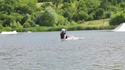 Mujer joven tirada por una cuerda de remolque se levanta y monta una tabla de wakeboard cerca de las rampas
