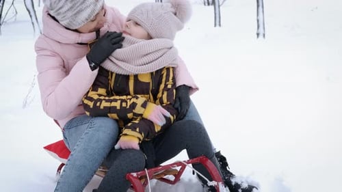 Loving Mother and Daughter on Sled in Snowy Woods