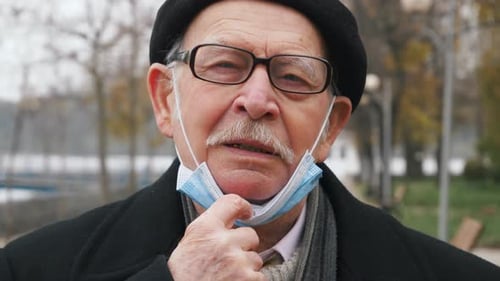 Senior Man Adjusts Mask Outside on Cloudy Day