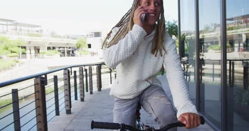 Mixed race man with dreadlocks riding a bicycle in the street talking on smartphone