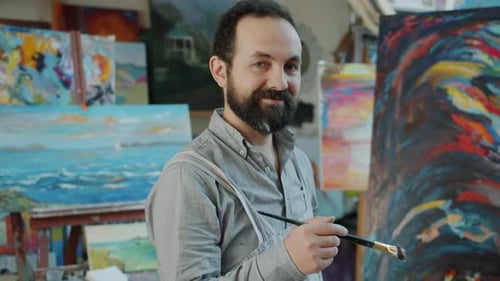 Portrait of Handsome Bearded Man Artist Standing in Studio Next To Abstract Picture