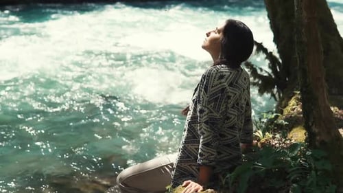 Die Frau kauerte neben dem einsamen Baum und dem schnellen Fluss, um sich auszuruhen