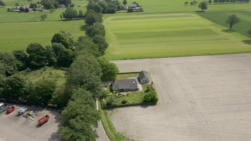 Aerial of small farm house near a harvested pasture surrounded by green meadows