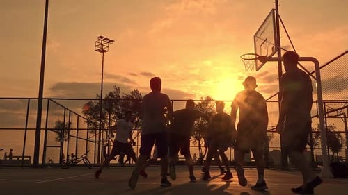 Junge Männer spielen Basketball bei Sonnenuntergang