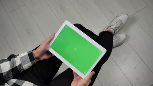 Mann sitzt auf einem Stuhl und schaut auf ein digitales Tablet mit Chroma-Key auf dem grünen Bildschirm