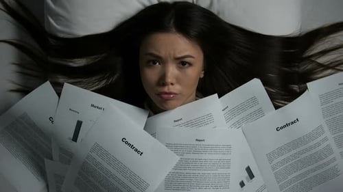 Young Asian Woman Covered With Pile of Documents Disappearing on Bed, Overwork