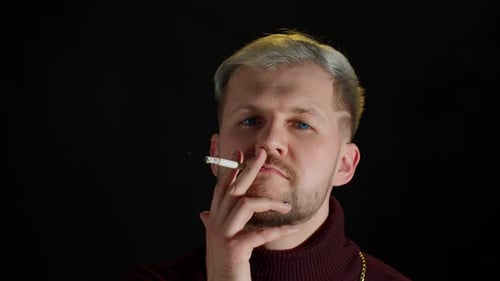 Stylish Addicted Young Man with Blue Eyes in Trendy Clothes Looking at Camera Smoking Cigarette