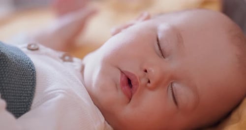 Close Up of Beautiful Sleeping Baby Under the Grey Blanket Who Turns Its Head Away From Camera