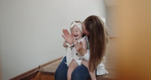 Mother Sits on the Stairs Holding Baby Daughter on Her Knees Playing with Her