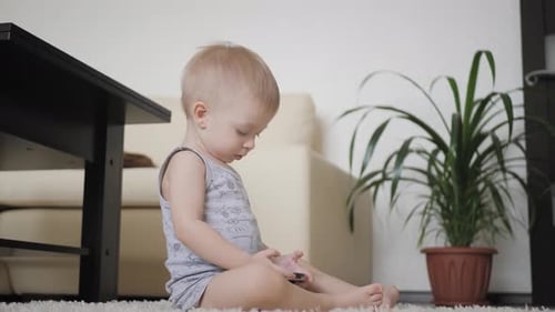 Child Sits on Rug Looking at Mobile Phone
