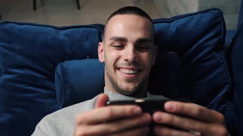Man Smiling While Looking at Smartphone on Couch