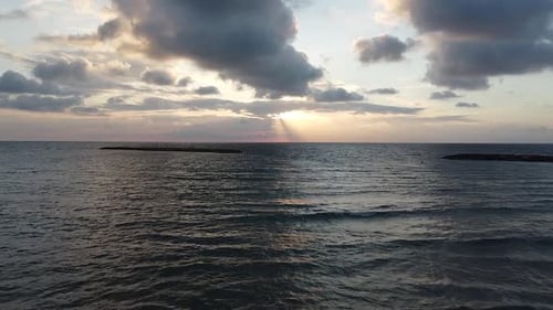 Aerial low fly toward the sunset over the clam dark sea, lines of clouds, drone shot