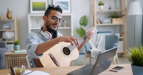 Young Adult Plays Guitar at Desk at Home