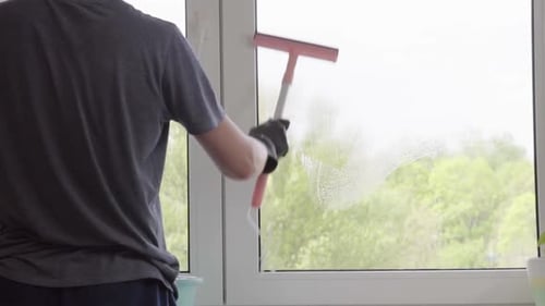 Adult Cleaning Window with Squeegee in Home