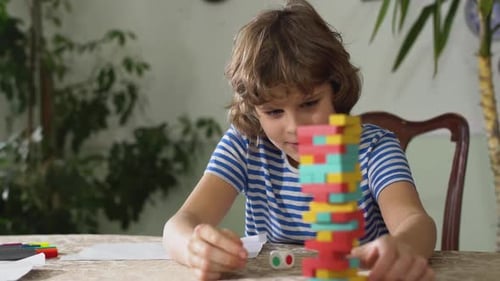 Small Adorable Cute Kid Sitting on the Table and Play Game Inside a Room. Boys Playing Jenga