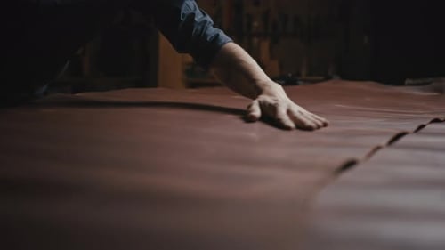 Unerkennbarer Schneider glättet Leder auf dem Tisch, um die Stoffqualität vor der Arbeit zu untersuchen