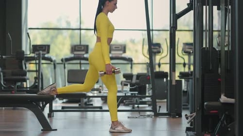 Sportive Woman is Doing Lunges for Legs with Dumbbells in Her Hands in Gym