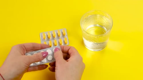 Hands Removing Pills Next to Glass of Water