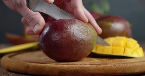 Männliche Hand mit einem Messer schneidet ein Stück frische Mango ab.